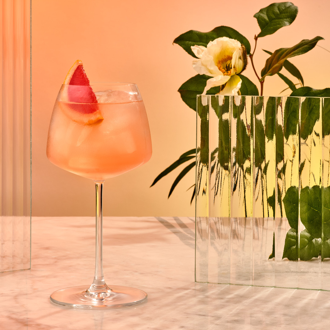 A light pink cocktail in a coupa glass with a blood orange wedge garnish