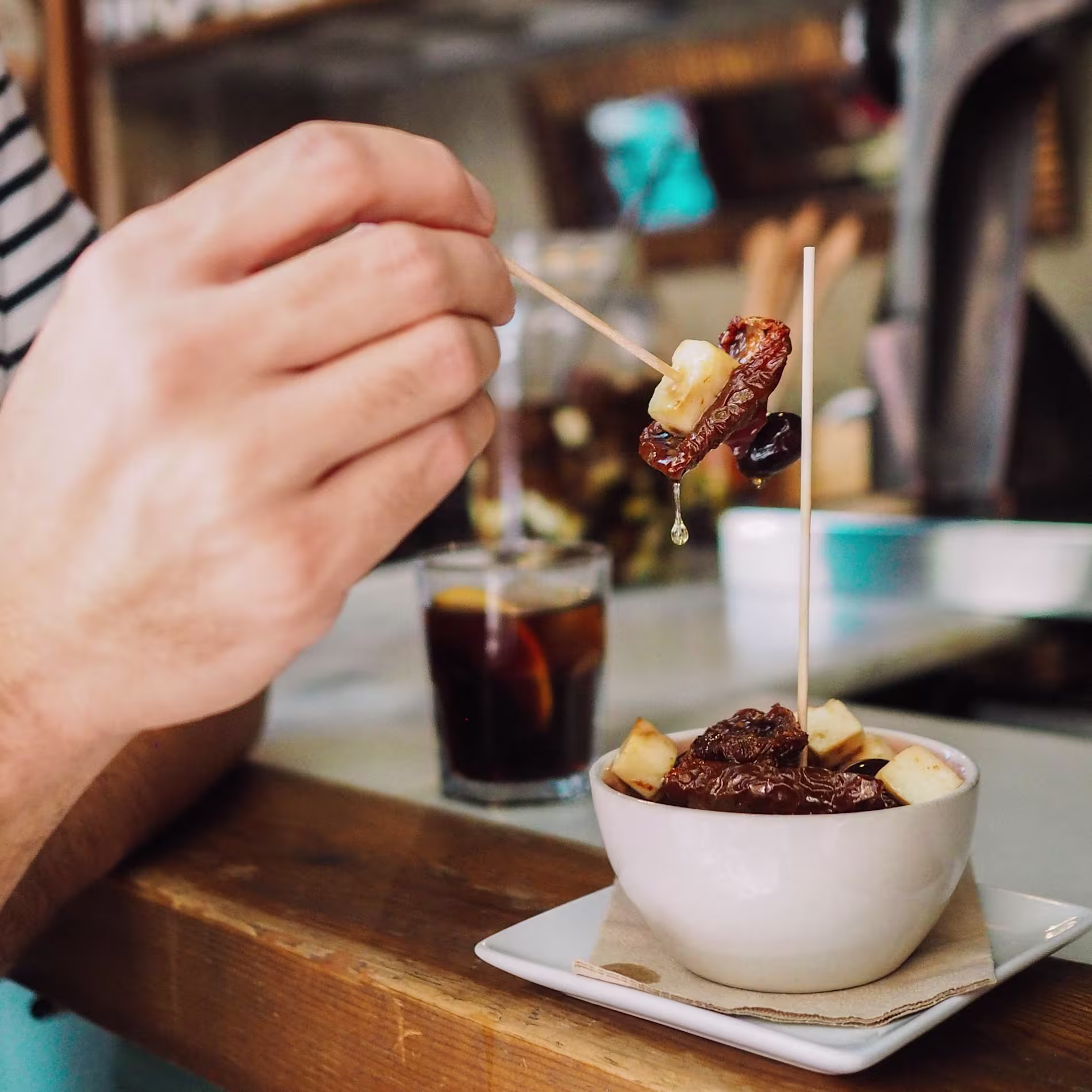 Brocheta de dátil con queso y vermut bien frío en barra de madera en Taberna La Senia, puro sabor en cada bocado.