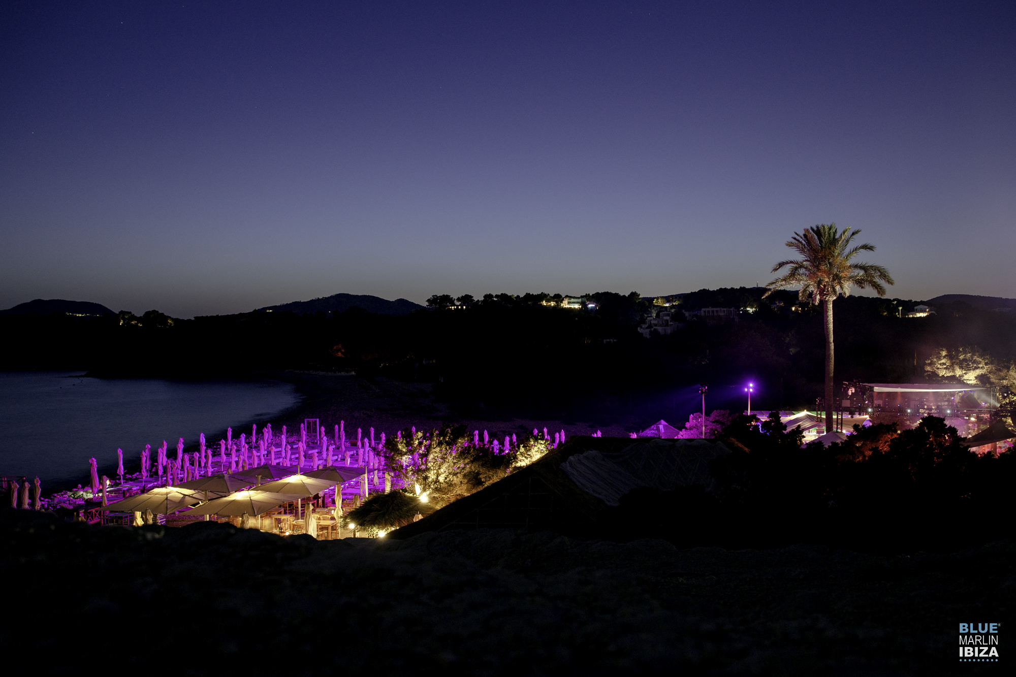 En Blue Marlin Ibiza, disfruta de la brisa marina y el ambiente vibrante de la playa mientras el lugar se ilumina al caer la noche.