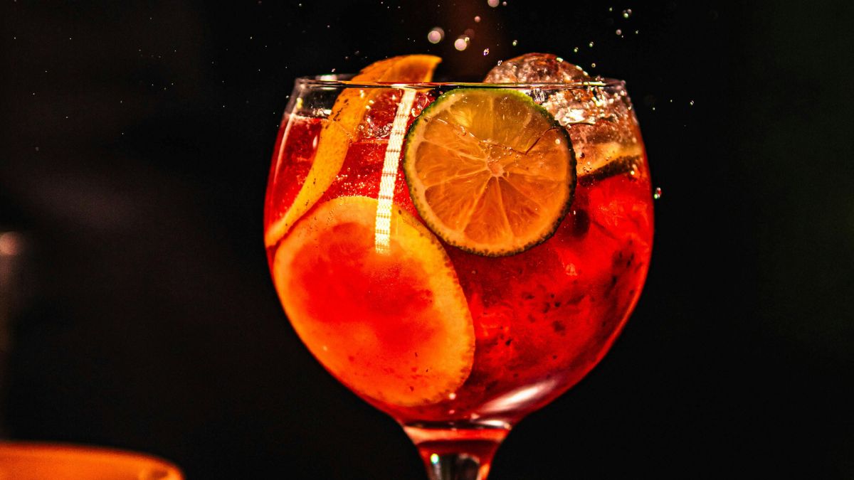A close up shot of a spritz cocktail in a glass, filled with fruit slices