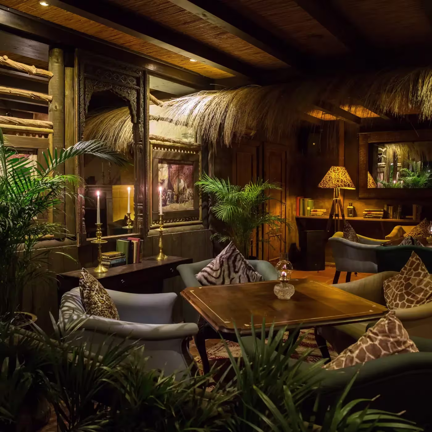 Ambiente cálido y exótico de Trocadero Sotogrande, con sofás elegantes, iluminación tenue, detalles de inspiración africana y abundante vegetación.
