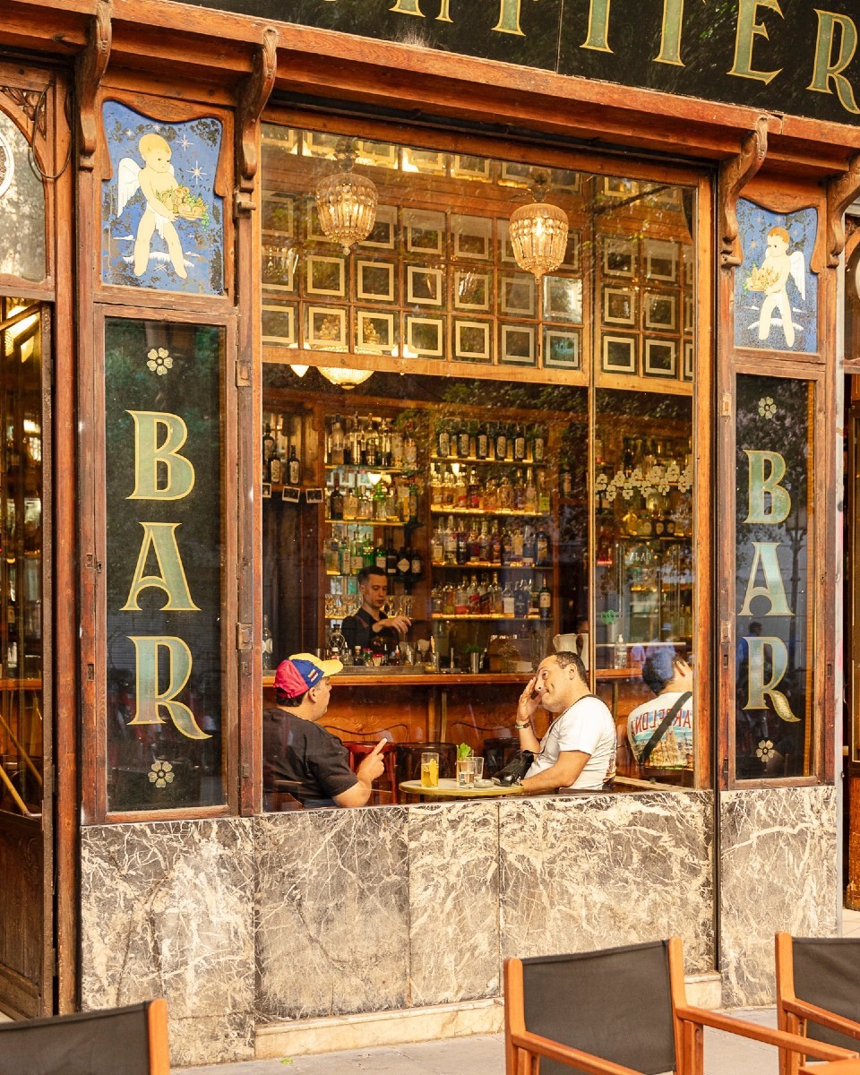 En La Confitería, su fachada clásica de madera y mármol enmarca un bar lleno de historia, con cristaleras que revelan un interior vibrante.