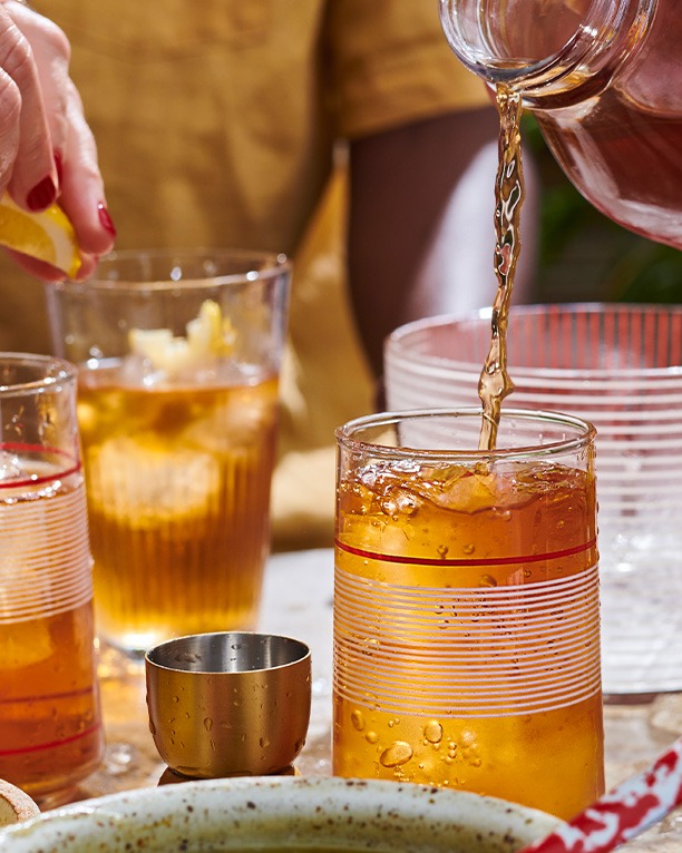 Someone pouring iced tea from a jug into different coloured glasses