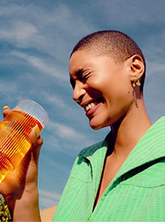 Smiling person enjoying a cocktail outdoors in bright lighting