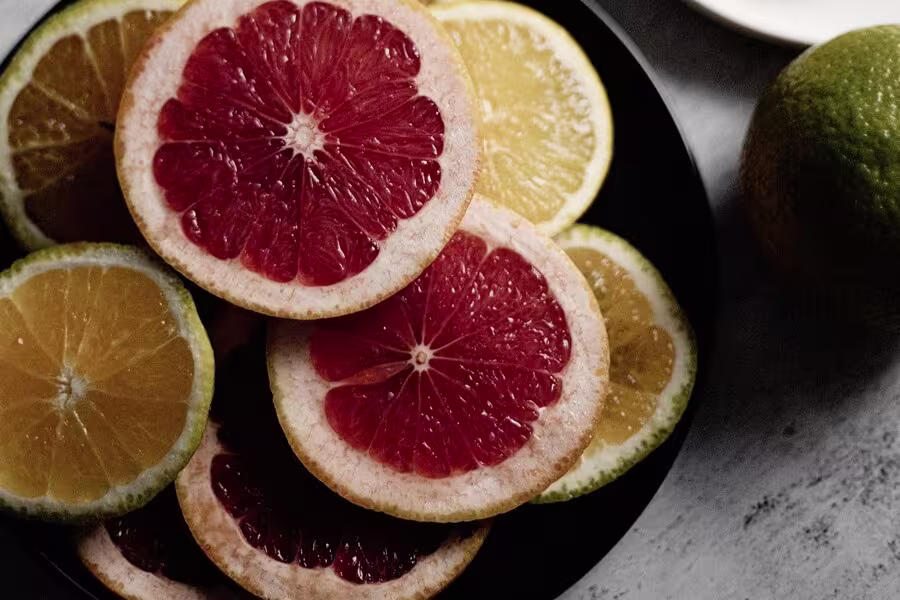 A black plate with slices of red grapefruit and yellow lemon, shown from above on a light surface.