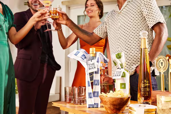 A group toast their glasses behind a table which sits an engraved bottle of Johnnie Walker and a bowl of potato chips.