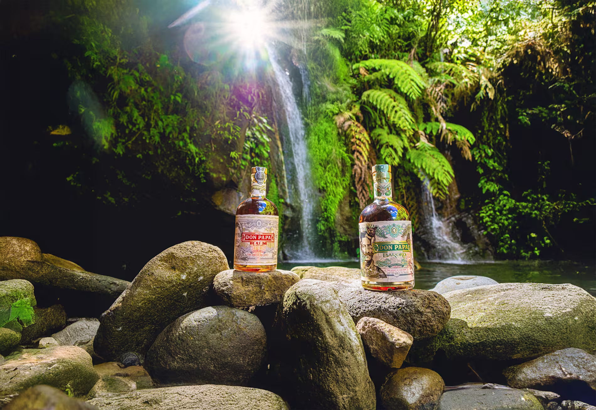 Botellas de ron Don Papa expuestas sobre unas rocas frente a una exuberante cascada y la vegetación