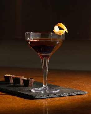 Rumos Manhattan koktél kupés pohárban, narancshéjjal díszítve.