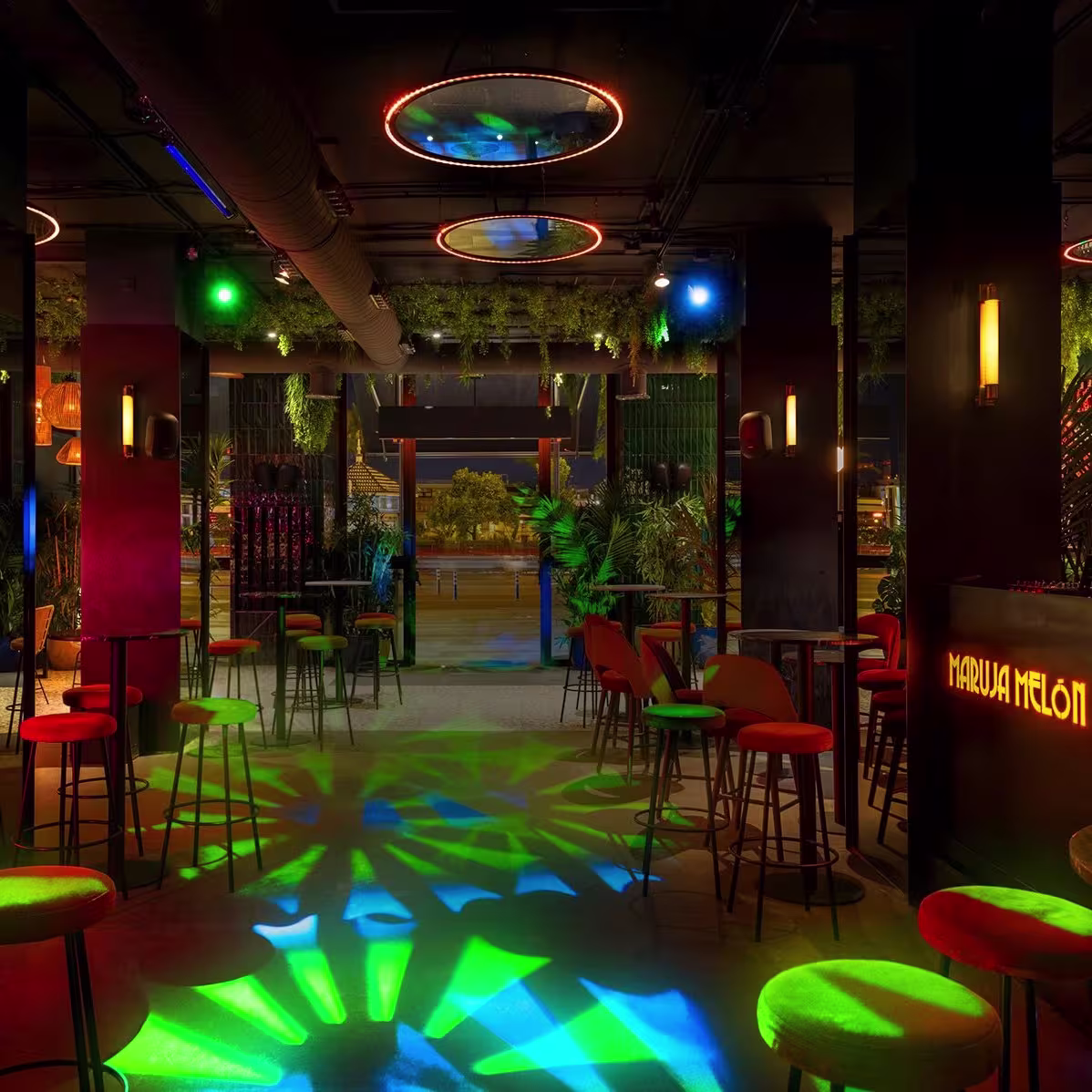 Luces de colores y vegetación crean un ambiente vibrante y tropical en el interior de Maruja Melón, listo para una noche de fiesta.