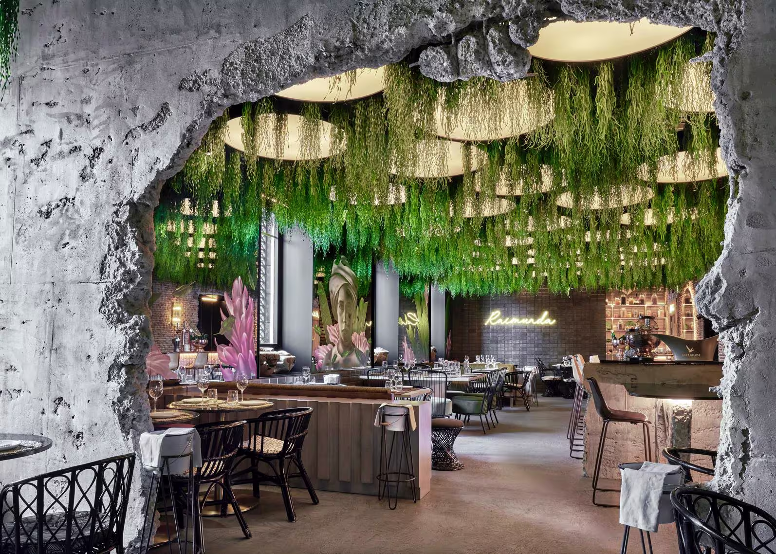 Interior de Raimunda con techos decorados con plantas colgantes, mesas elegantes, luz tenue y un ambiente tropical sofisticado.