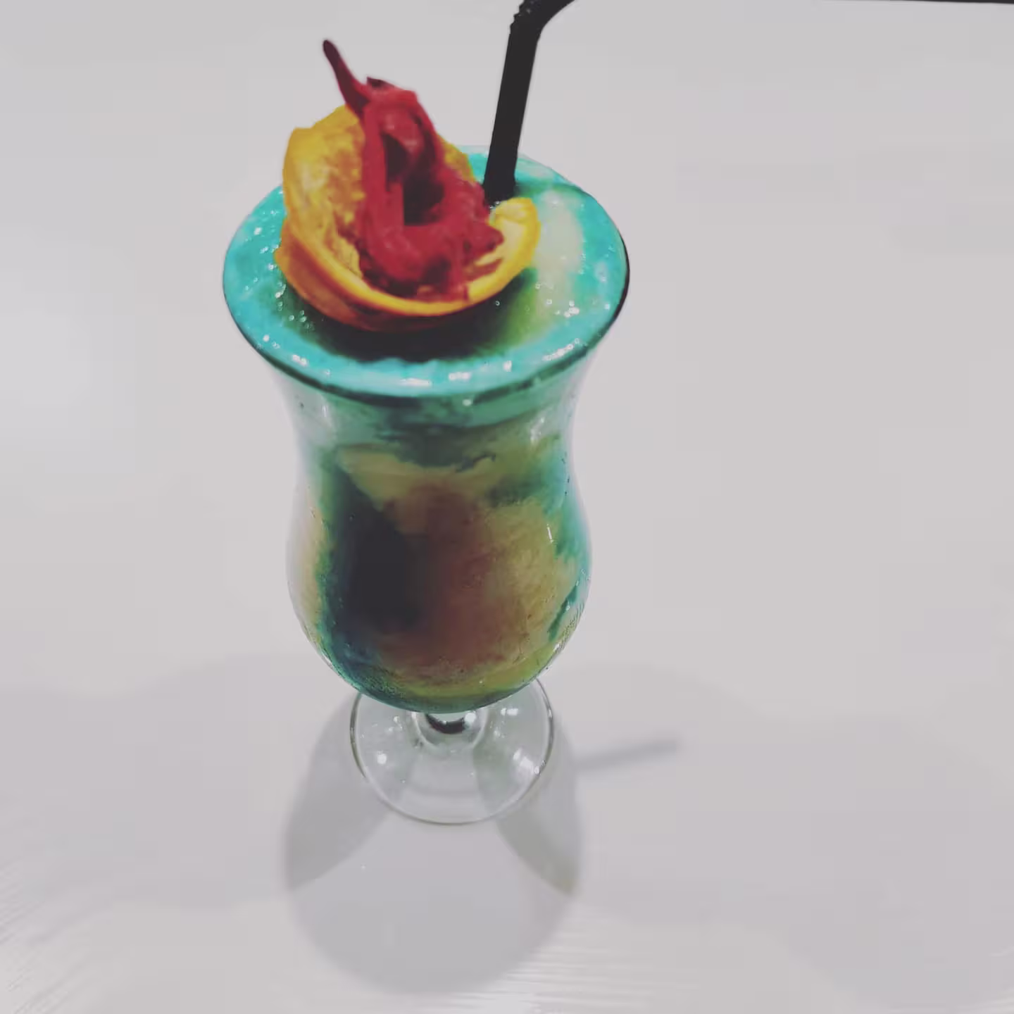 Cóctel colorido en Artadi Beach con tonos azules, decoración de frutas y pajita negra. Ambiente refrescante y tropical.