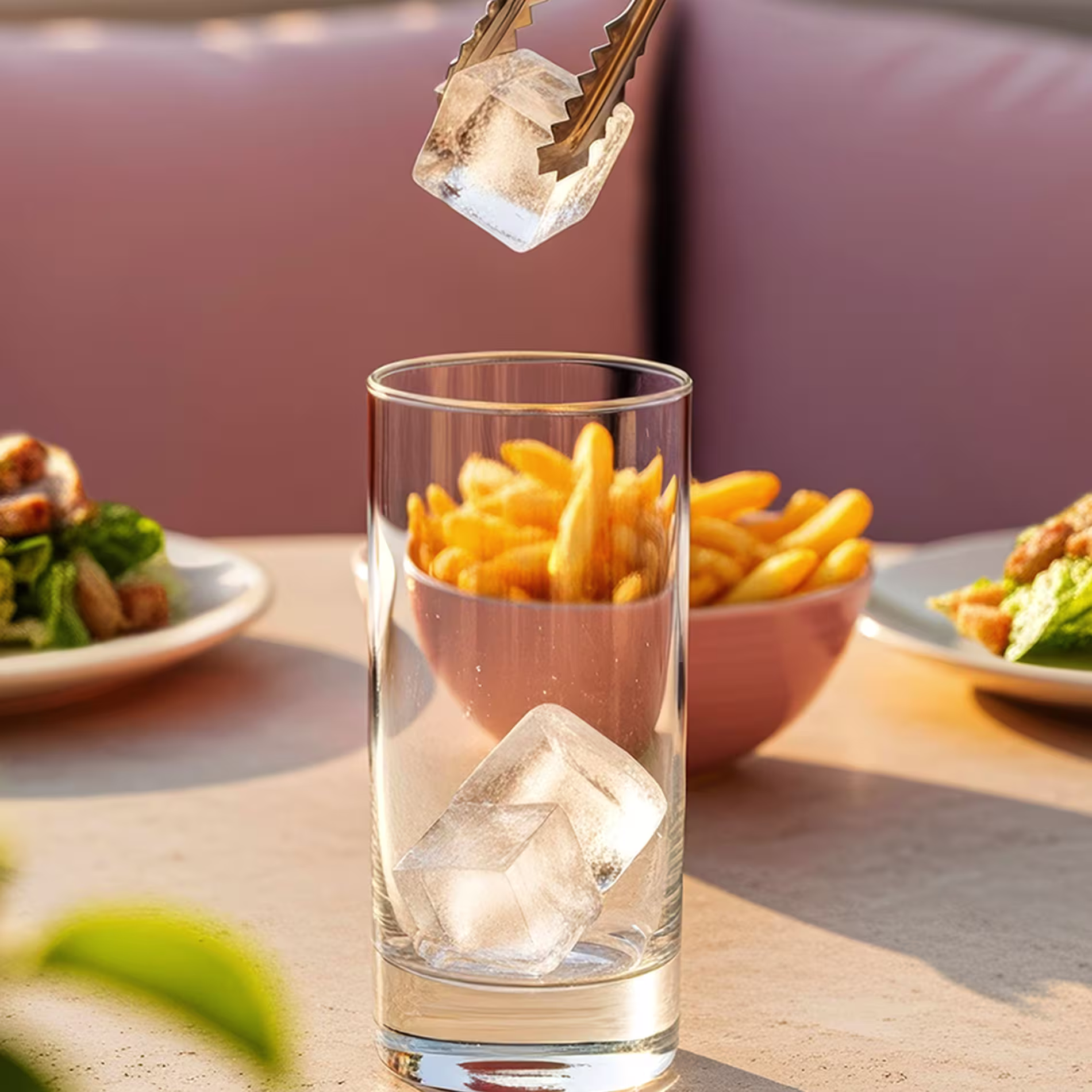 Ice is added to a highball glass using metal tongs