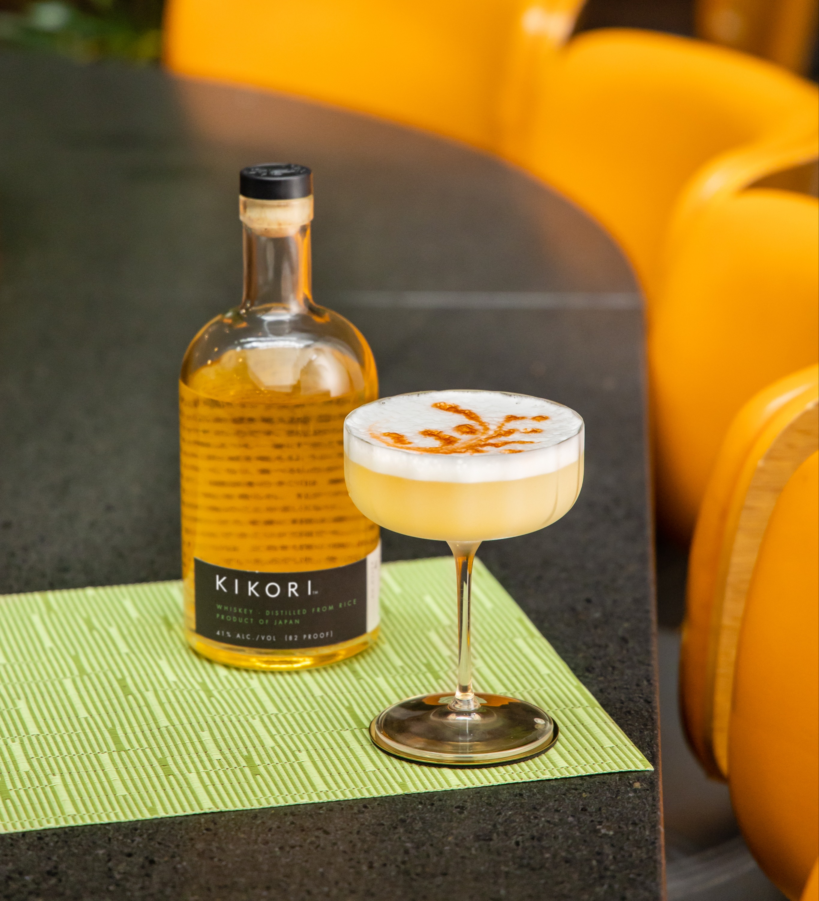 Kikori Chai Whiskey Sour cocktail served beside a bottle of Kikori Whiskey and garnished with spice.