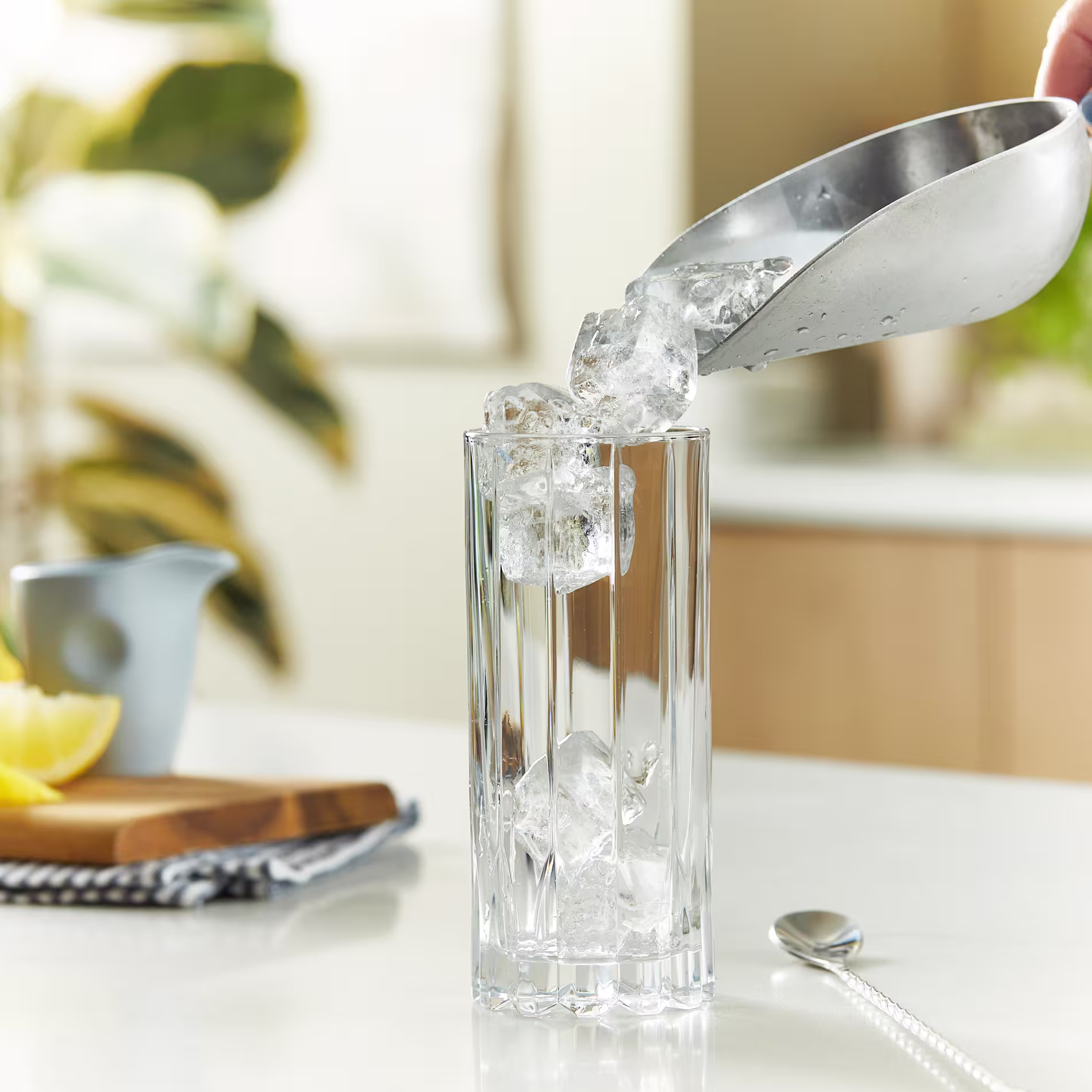 Ice is poured into a highball glass using a silver bar scoop