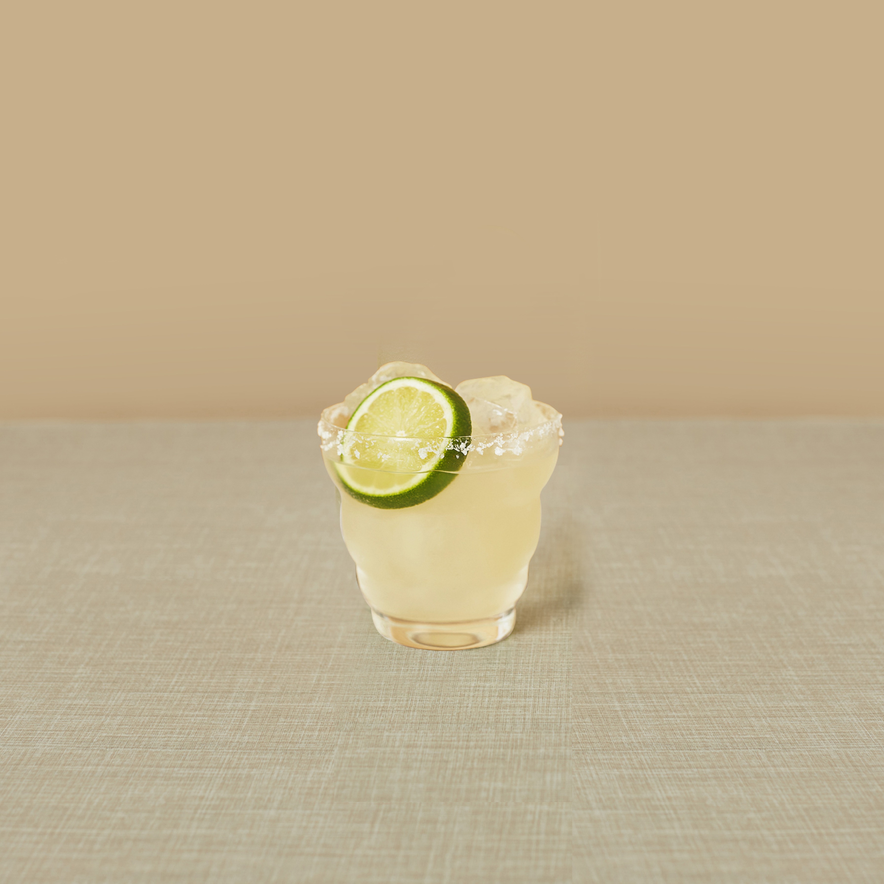 O margarita într-un pahar de whisky cu o felie de lămâie verde, lângă o sticlă de Seedlip Grove 42.