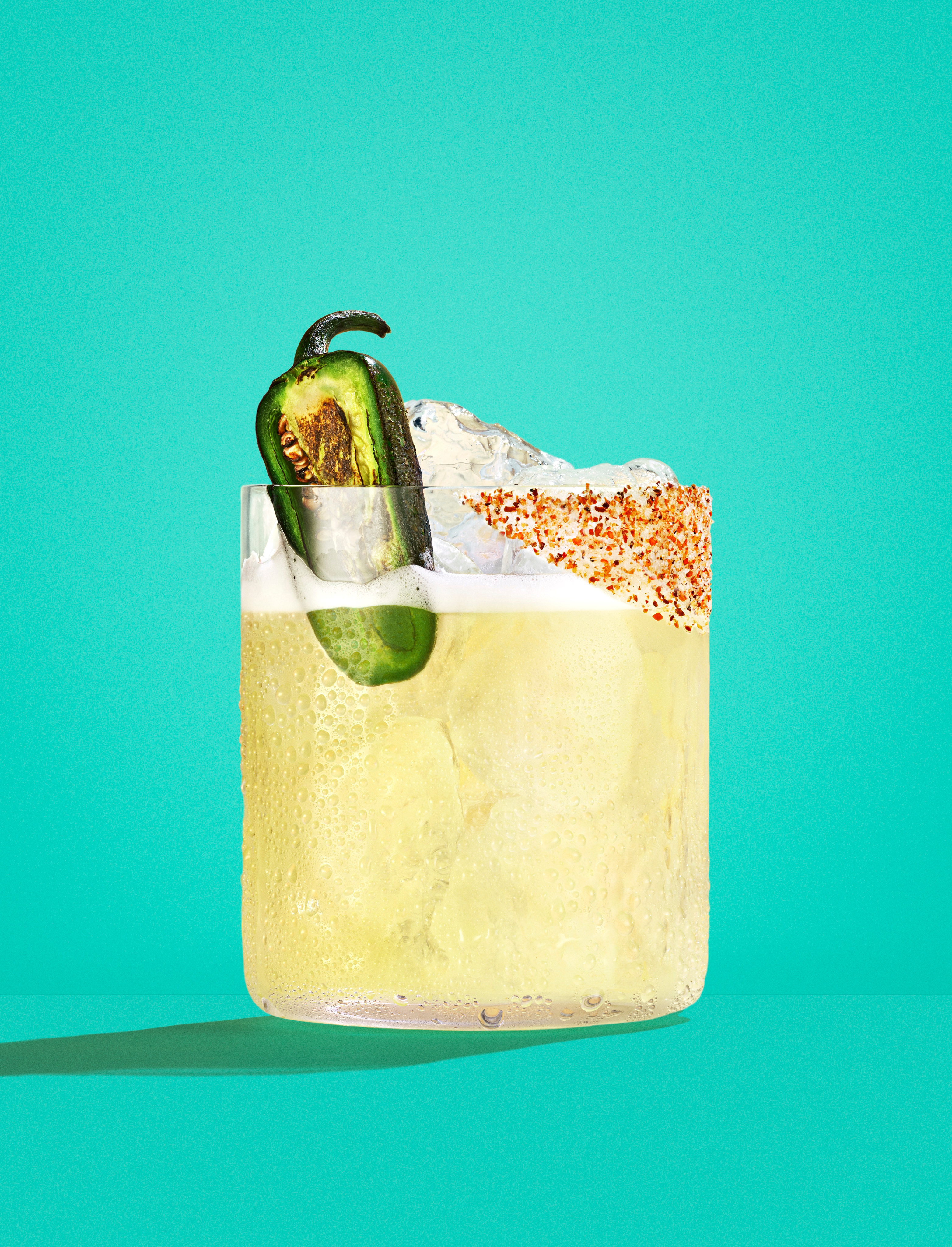 Casamigos tequila cocktail with ice, grilled jalapeño garnish, and chili salt rim on a turquoise background