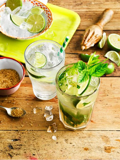 Spiced mojito garnished with mint and lime, served alongside ingredients like brown sugar and lime wedges on a rustic wooden table.