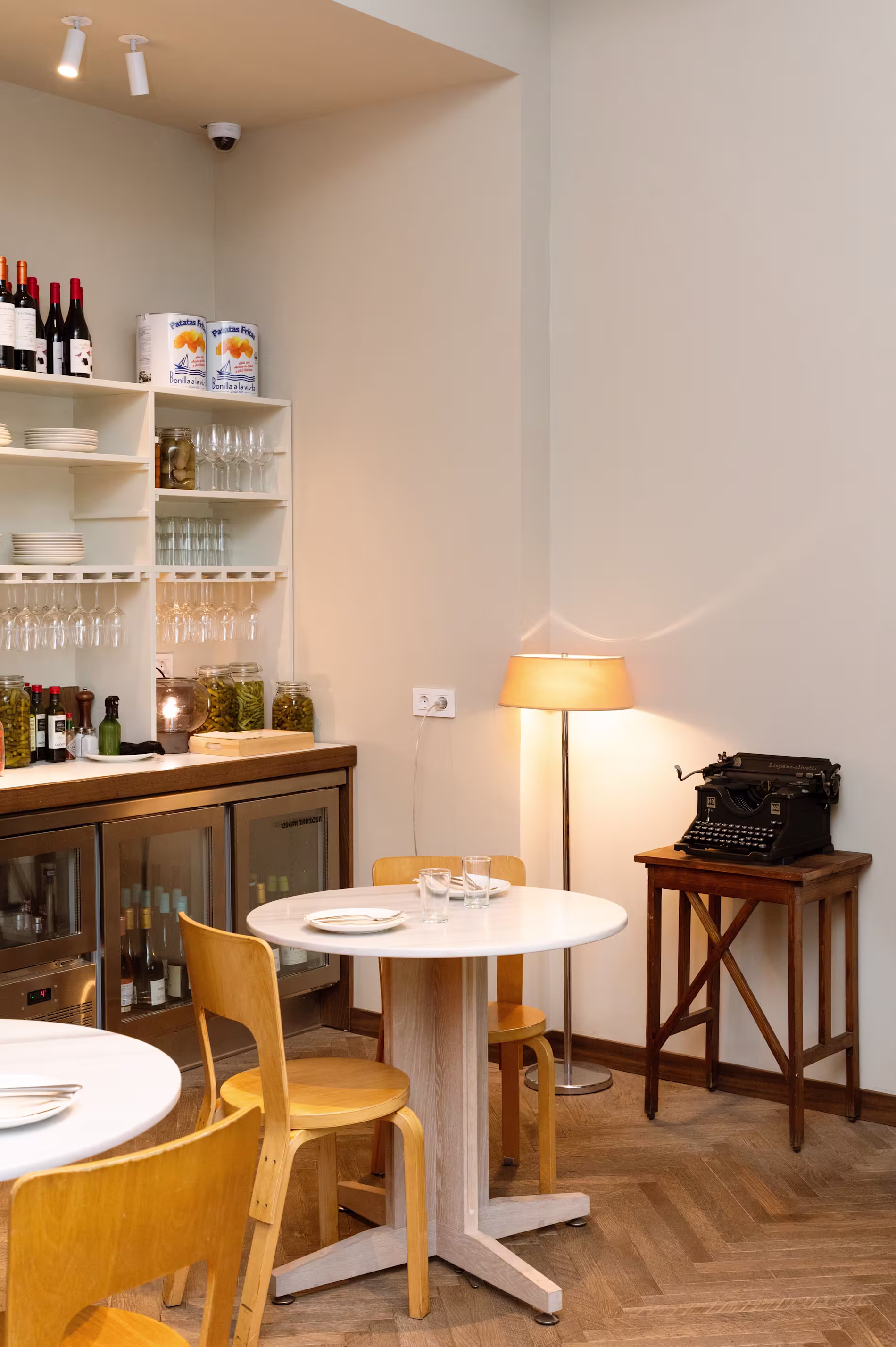 Rincón acogedor en Bar Bauma con una decoración minimalista, muebles de madera, una máquina de escribir vintage y estanterías con vinos y conservas.