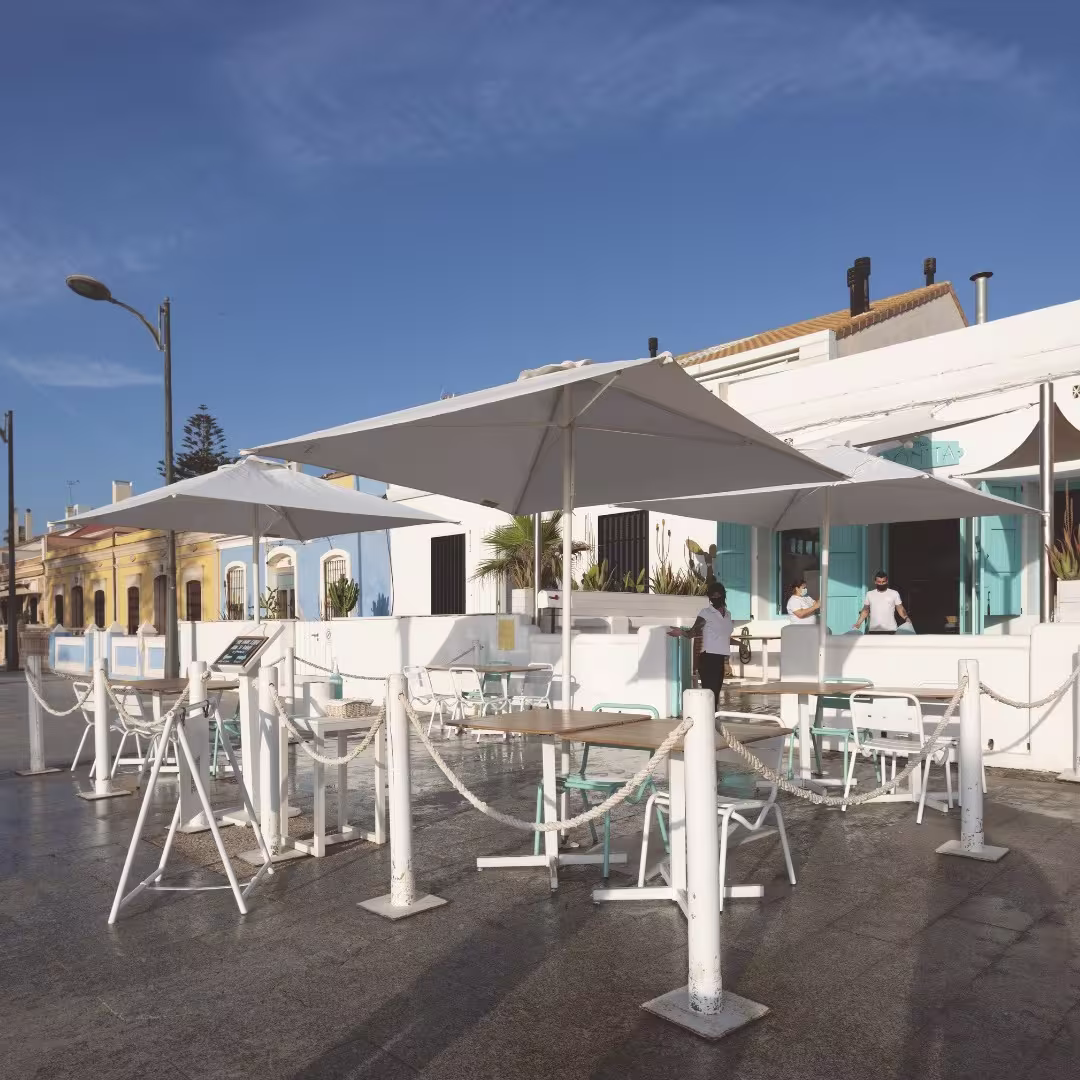 Sombrillas blancas, sillas turquesa y luz mediterránea en la terraza de La Más Bonita. Ideal para un desayuno frente al mar.