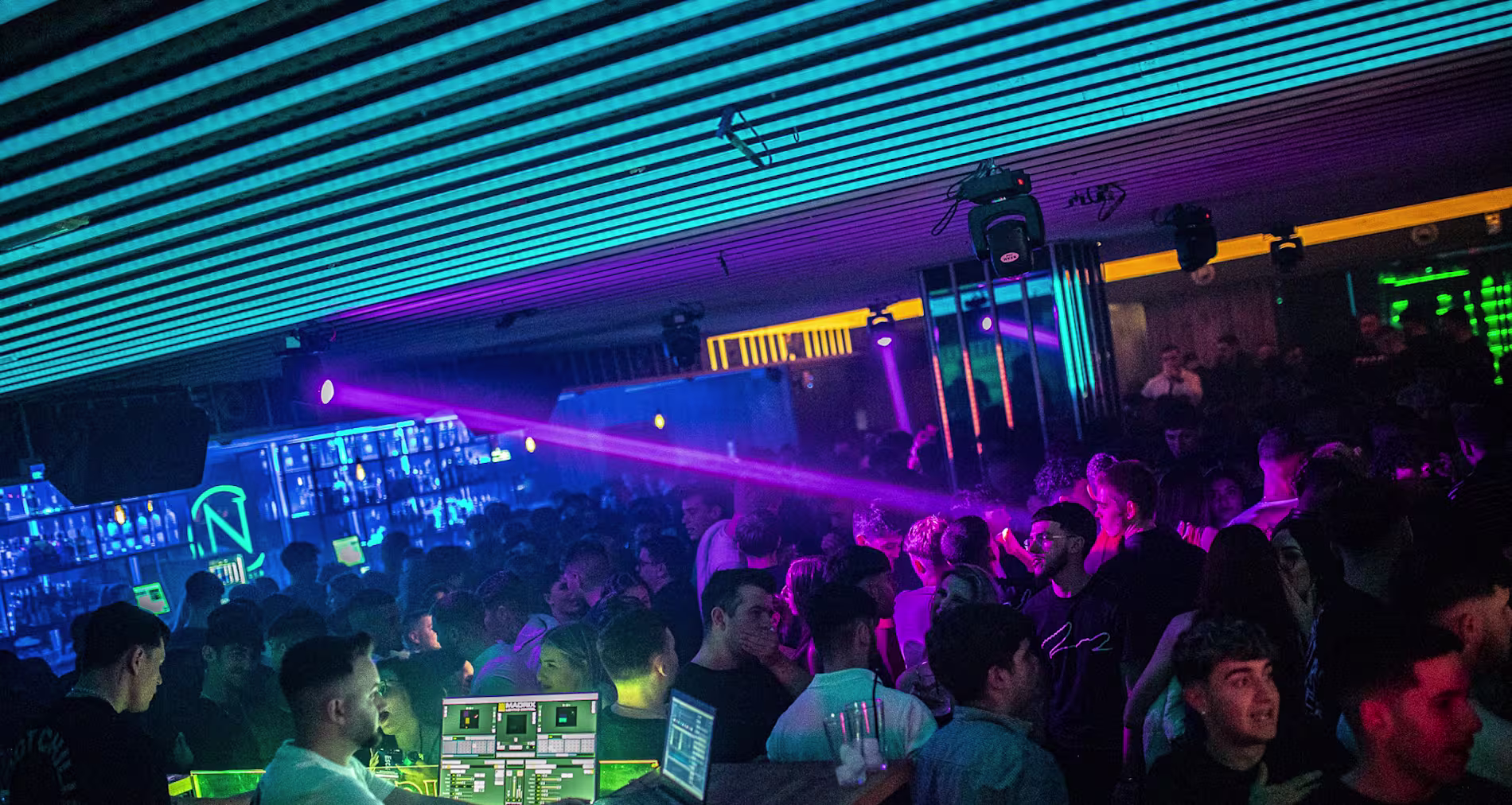 Coltán y Benavente con luces neón, DJ en acción y una multitud animada, creando una noche vibrante y llena de ritmo.