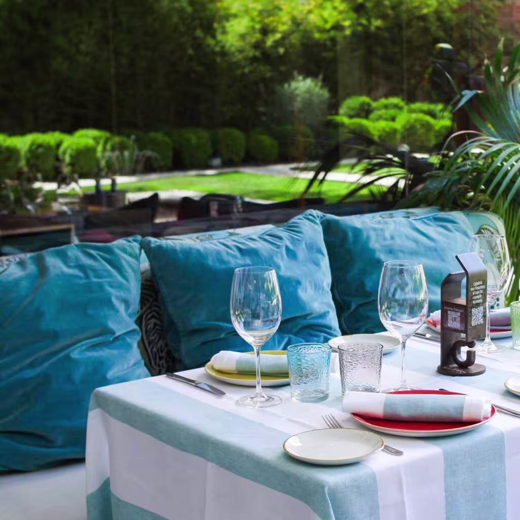 Terraza de Urrechu de Velázquez, con mesas preparadas, cojines azules y vistas a un jardín tranquilo y elegante.