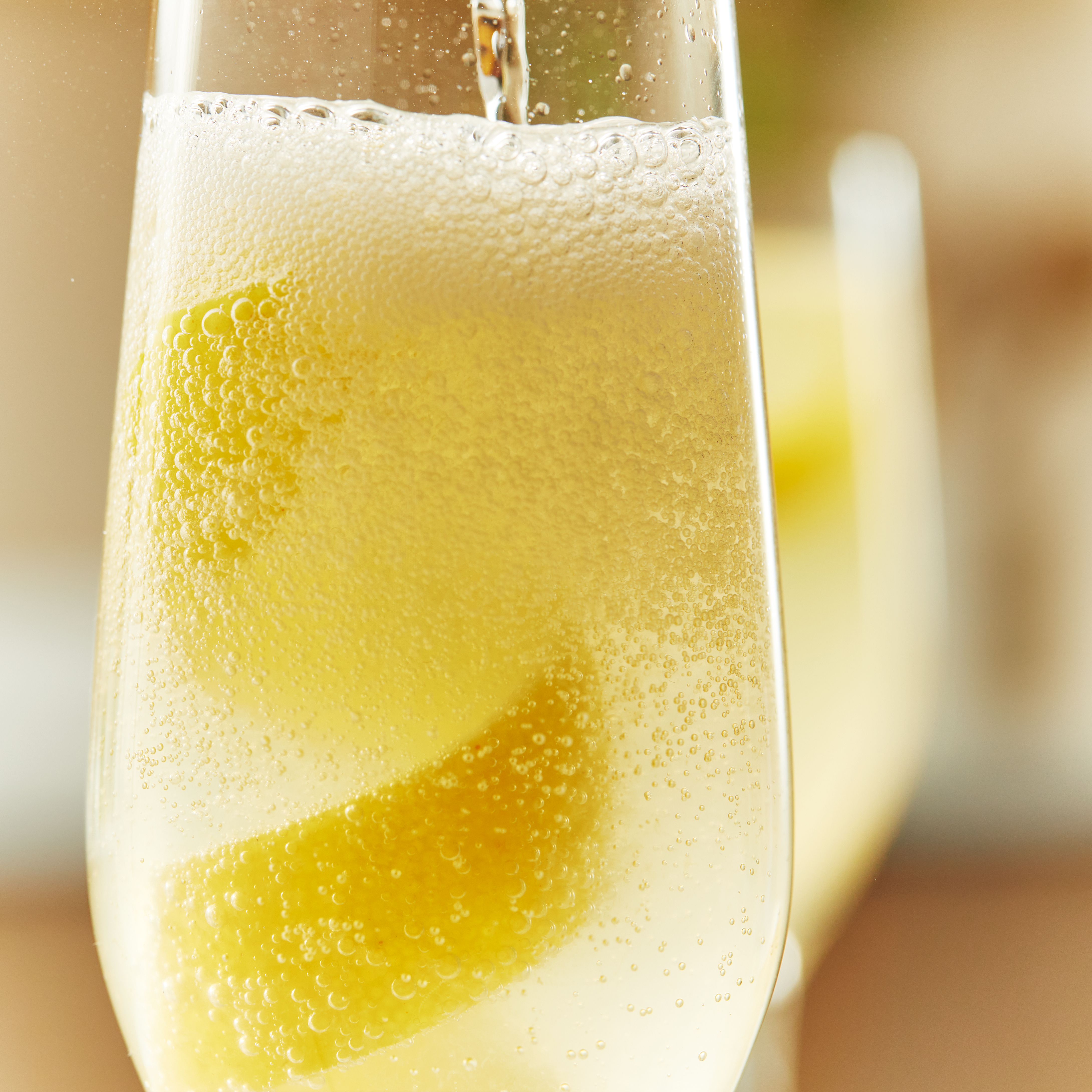 Fizzy liquid is poured into a Champagne flute with a large twisted lemon peel. F