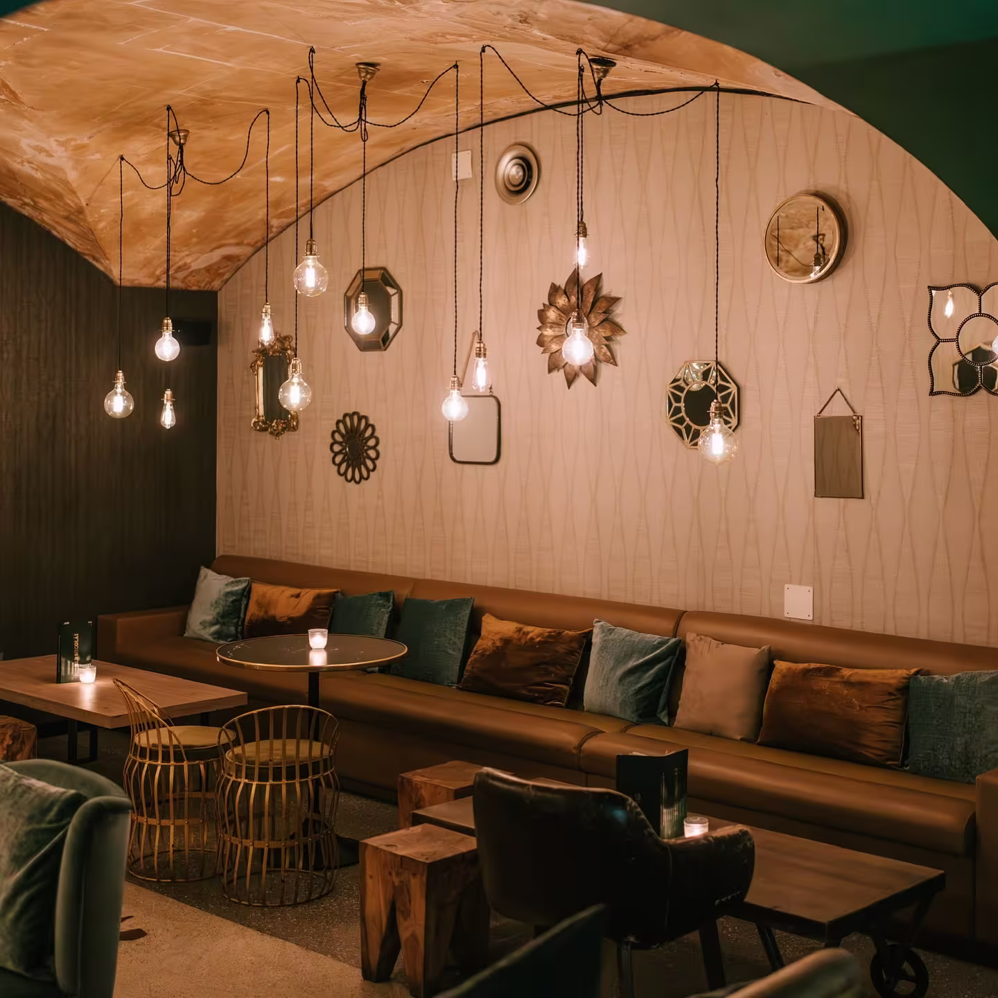 Interior de Bar Nicolás, con iluminación cálida y colgante, sofás de cuero, cojines en tonos cálidos y detalles decorativos elegantes en las paredes.