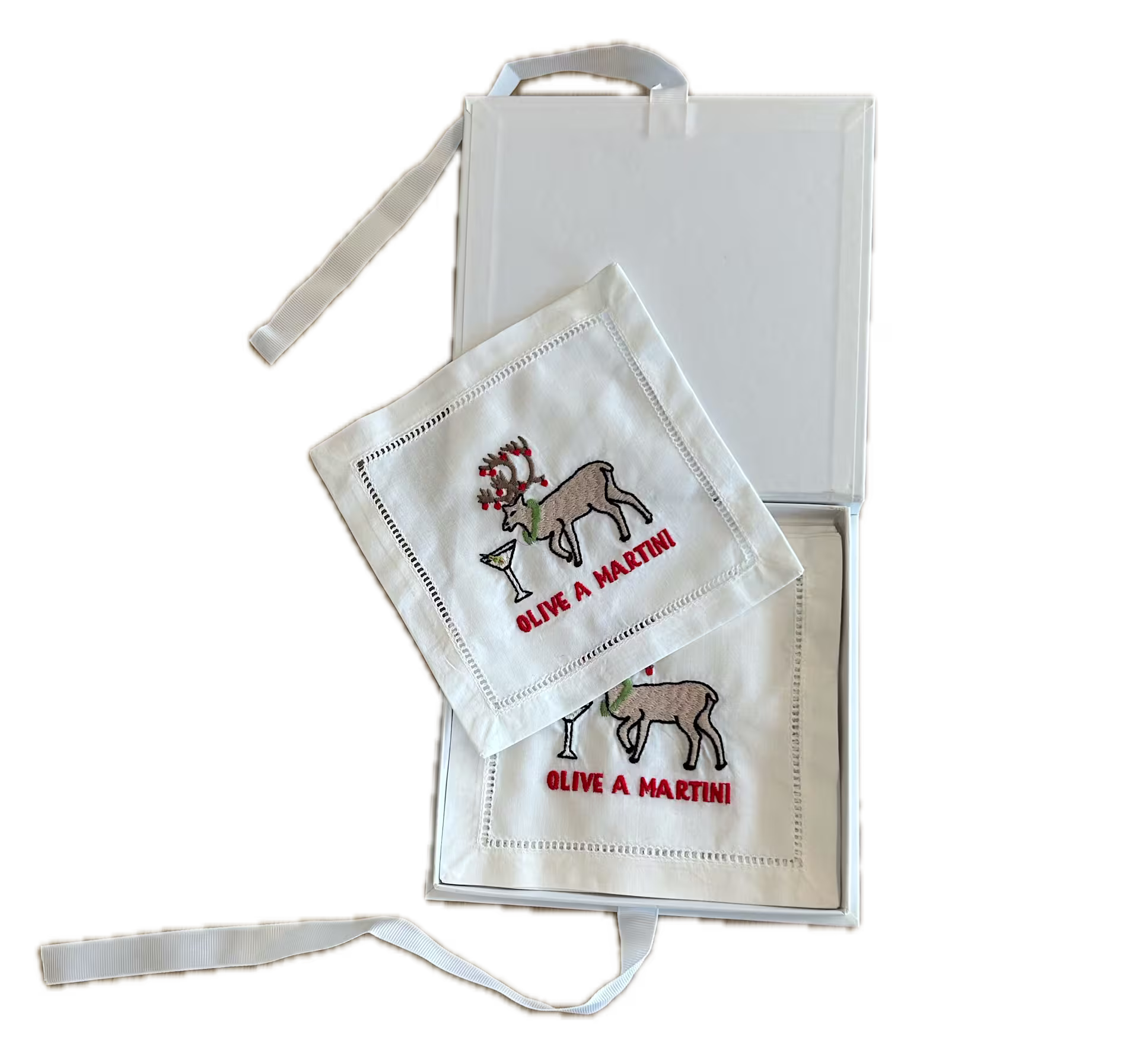 Two white cocktail napkins, each embroidered with a reindeer, a martini glass, and the words OLIVE A MARTINI, displayed with an open white box.