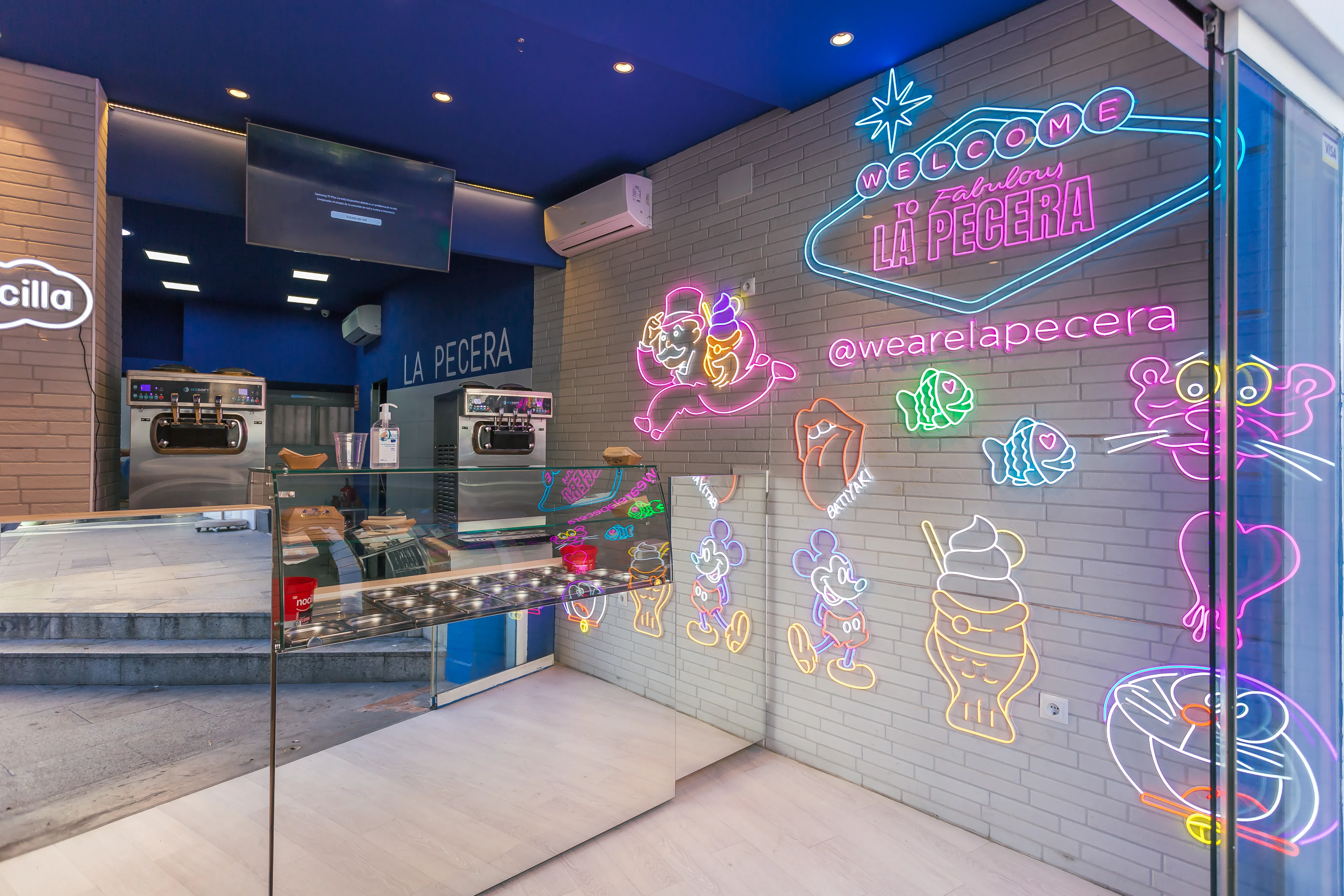Interior vibrante de La Pecera con neones coloridos, heladeras industriales y estética pop que invita a disfrutar helados únicos con estilo.