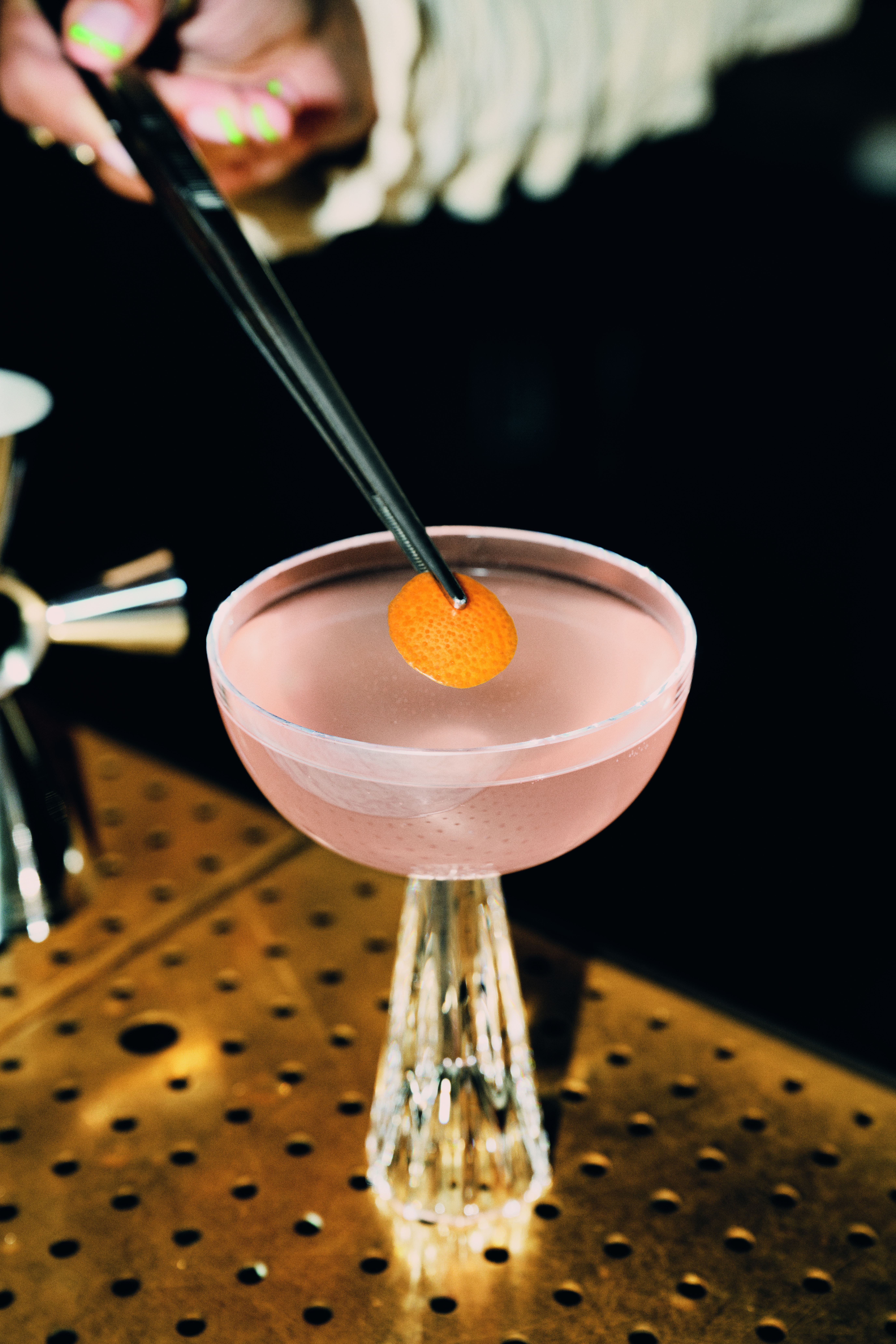 A light pink cocktail in a coupe glass with a small orange peel disc as a garnish
