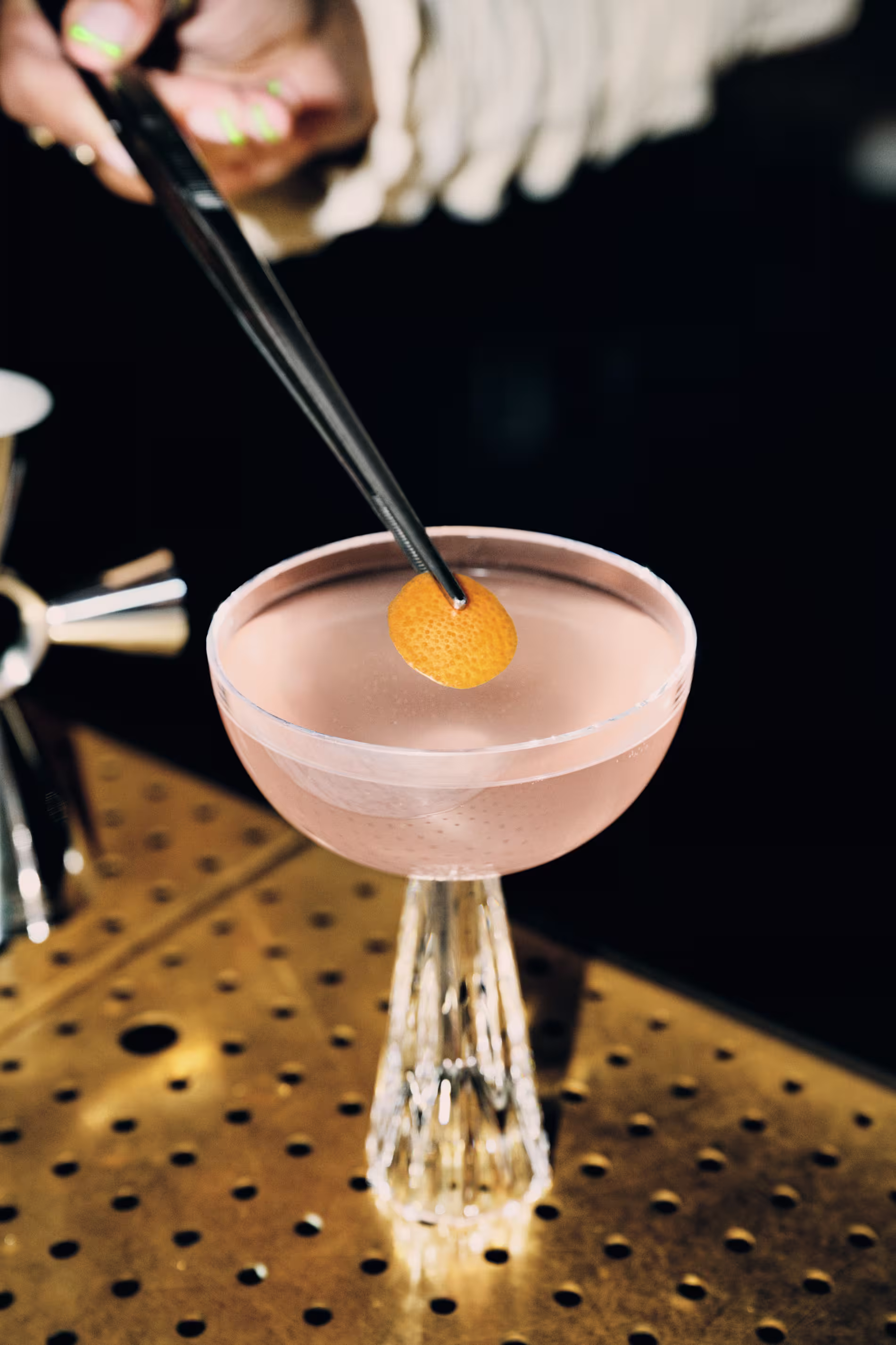 A light pink cocktail in a coupe glass with a small orange peel disc as a garnish