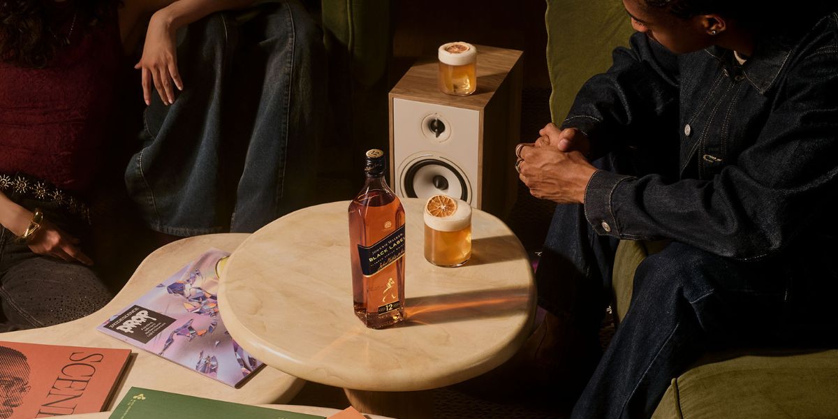 A group of people seated at a bar raise their glasses of a light-colored drink in a celebratory toast.