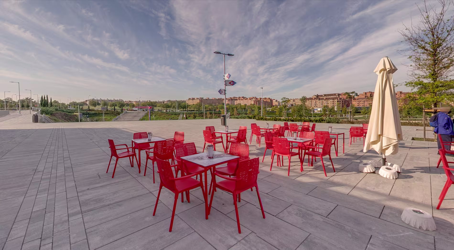 Terraza al aire libre con mesas y sillas rojas frente al estadio Wanda Metropolitano en Madrid, bajo un cielo despejado.