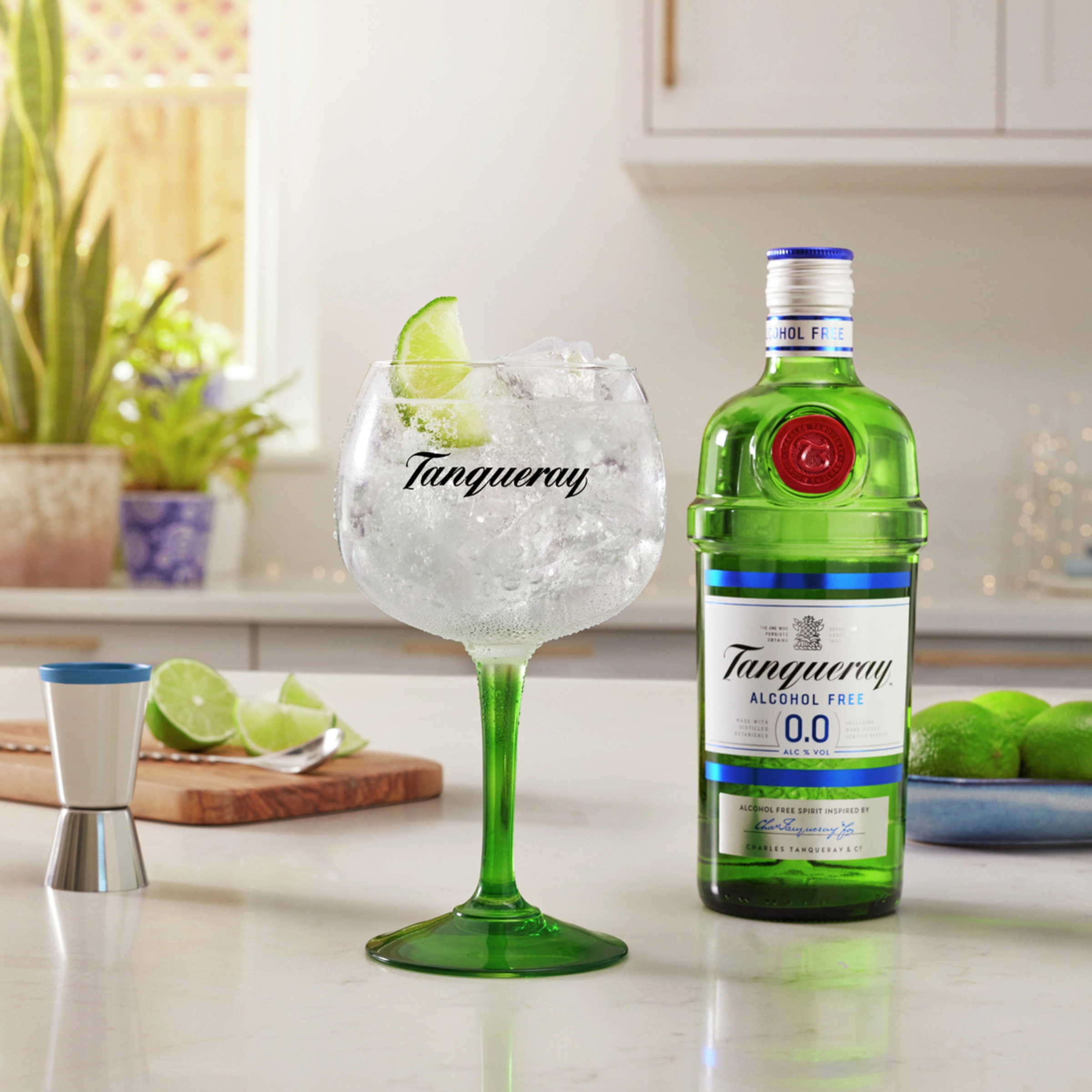 Copa de gin tonic con hielo y lima junto a una botella de Tanqueray sin alcohol en una cocina
