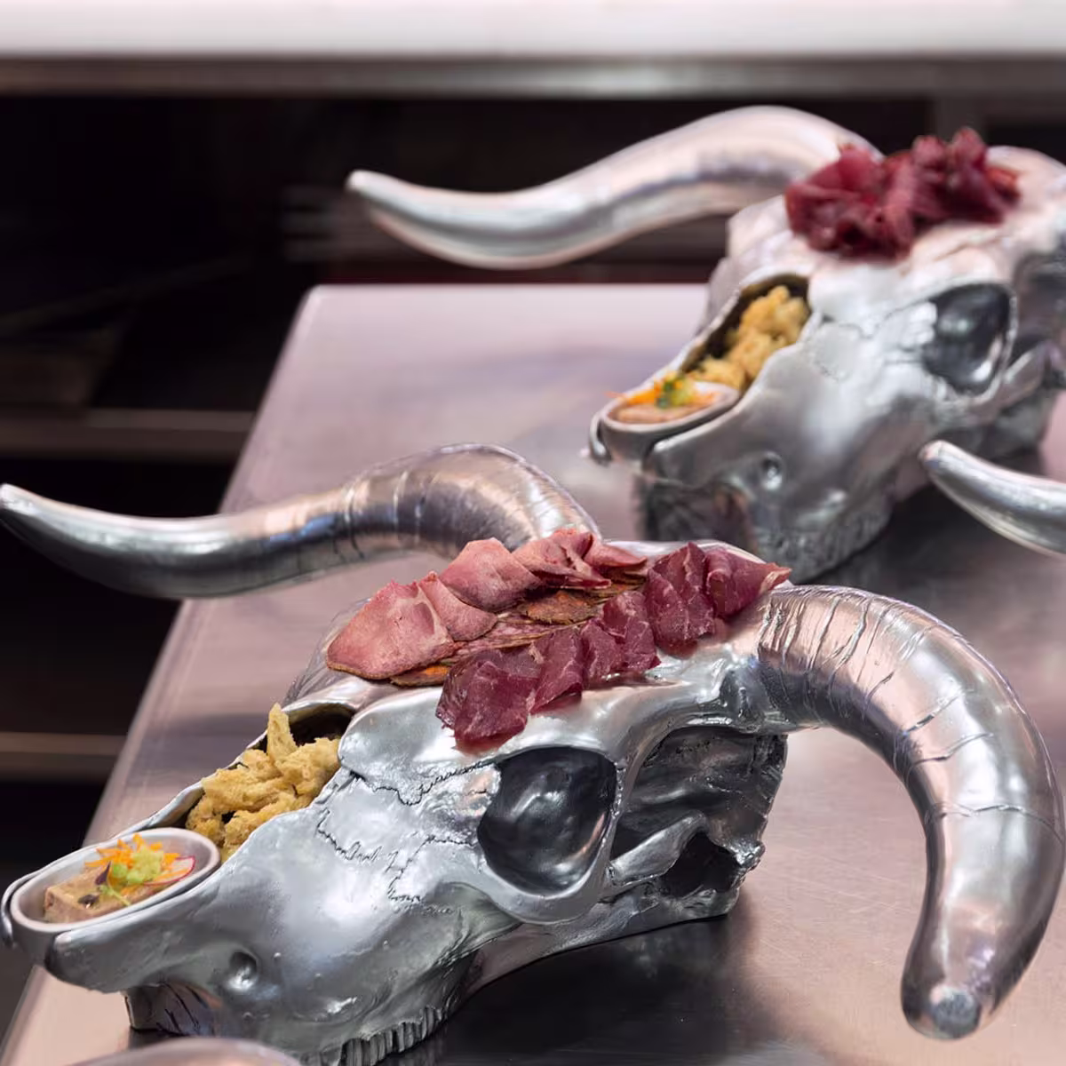 Presentación única en Lomo Alto, con platos servidos sobre cráneos metálicos de toro, decorados con embutidos selectos y guarniciones.