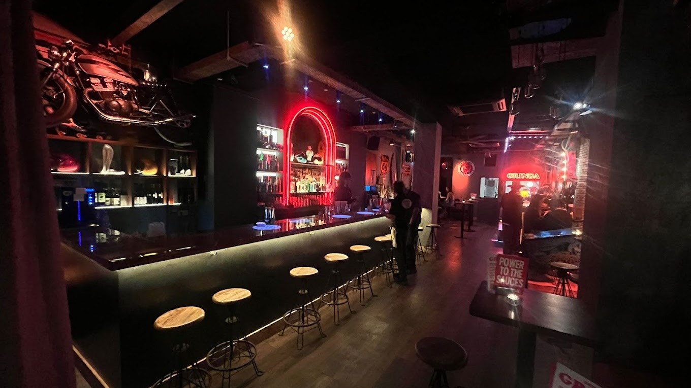 Bar con estética industrial, luces de neón, taburetes metálicos y una moto colgada que preside el ambiente. Espíritu rebelde, vibrante y nocturno.