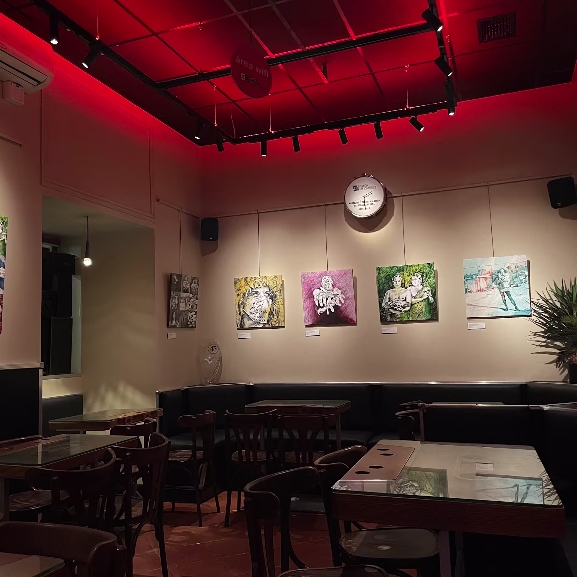 Sala de exposiciones en Café La Palma, con arte contemporáneo en las paredes y mesas dispuestas para los asistentes.