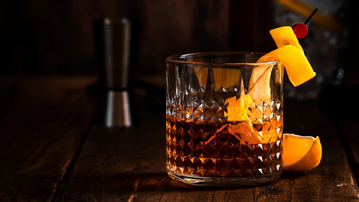 A man and woman enjoy Rum Old Fashioned cocktails, with a bottle of Zacapa rum on the table