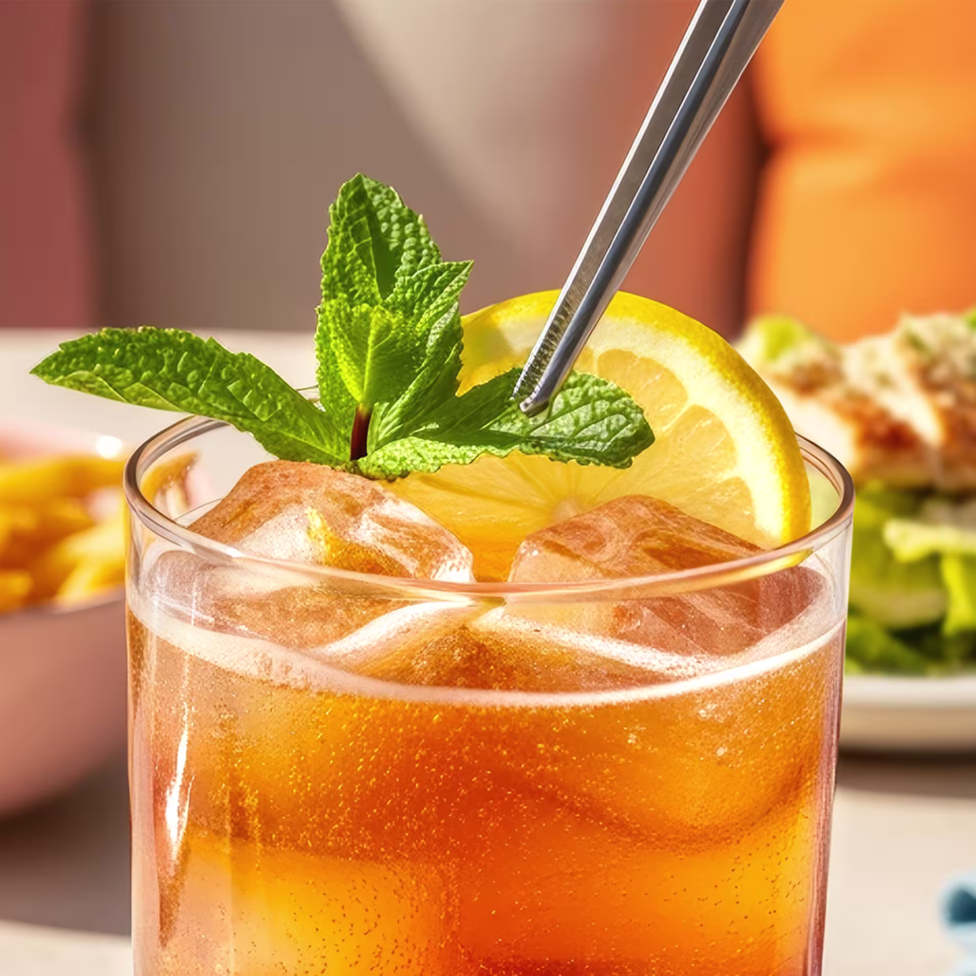Metal tongs placing a lemon wheel and mint sprig at the top of an Arnold Palmer cocktail