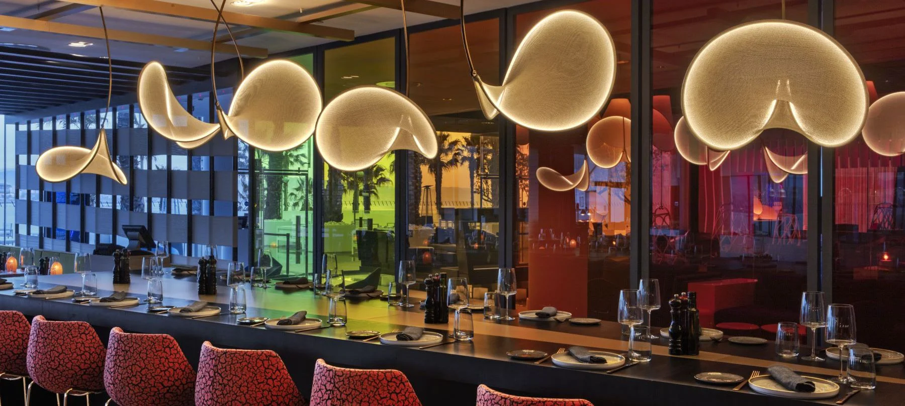 En Fire, W Hotel, una barra moderna con lámparas doradas y vistas al mar crea un ambiente sofisticado entre palmeras y luces cálidas.