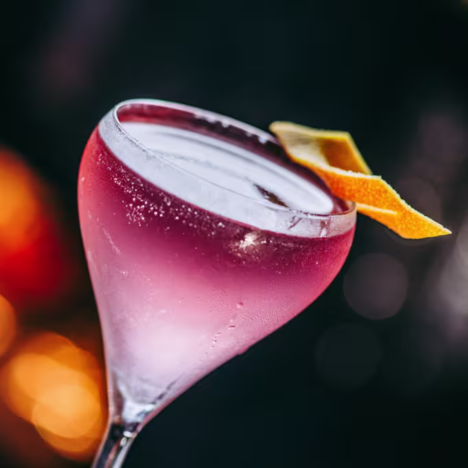 Un cóctel refrescante y vibrante en Mudanzas, con tonos rosados y un delicado twist de cítricos, perfecto para una noche especial.