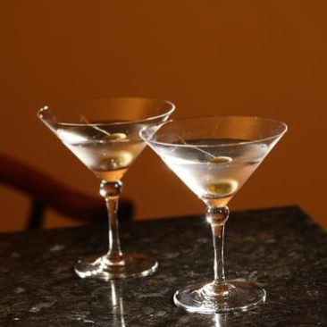 Two martini glasses with olives on picks sit on a bright red surface, casting shadows.