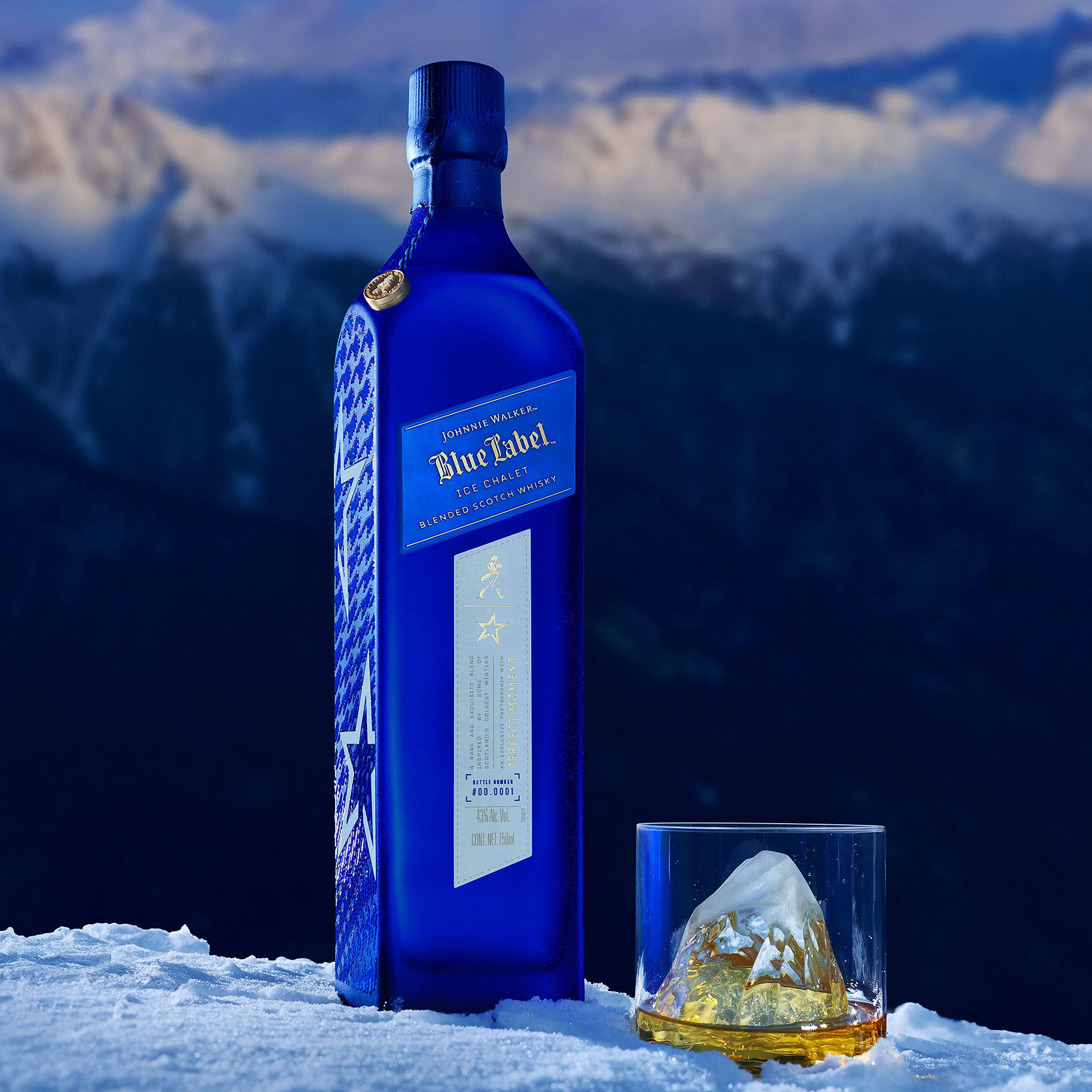 A blue bottle of Johnnie Walker Blue Label and a glass of whisky with ice are placed in front of a snow-covered mountain backdrop. Text above reads, Johnnie Walker Ice Chalet.