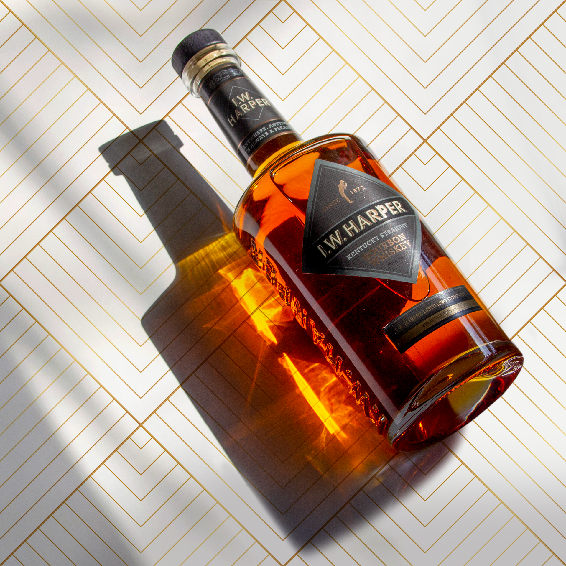 A bottle of I.W. Harper Kentucky Straight Bourbon Whiskey lies on a geometric white and gold surface, casting a shadow and reflection.