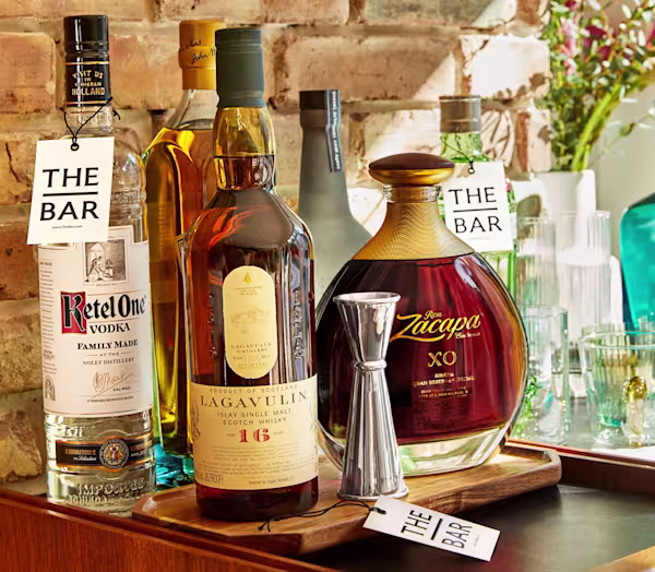 Bottles of Ketel One, Lagavulin, Zacapa sit on a table with labels displaying The Bar brand name.