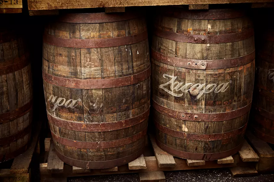 Two wooden barrels with metal bands, marked Zacapa, rest on wooden pallets under a shelf.