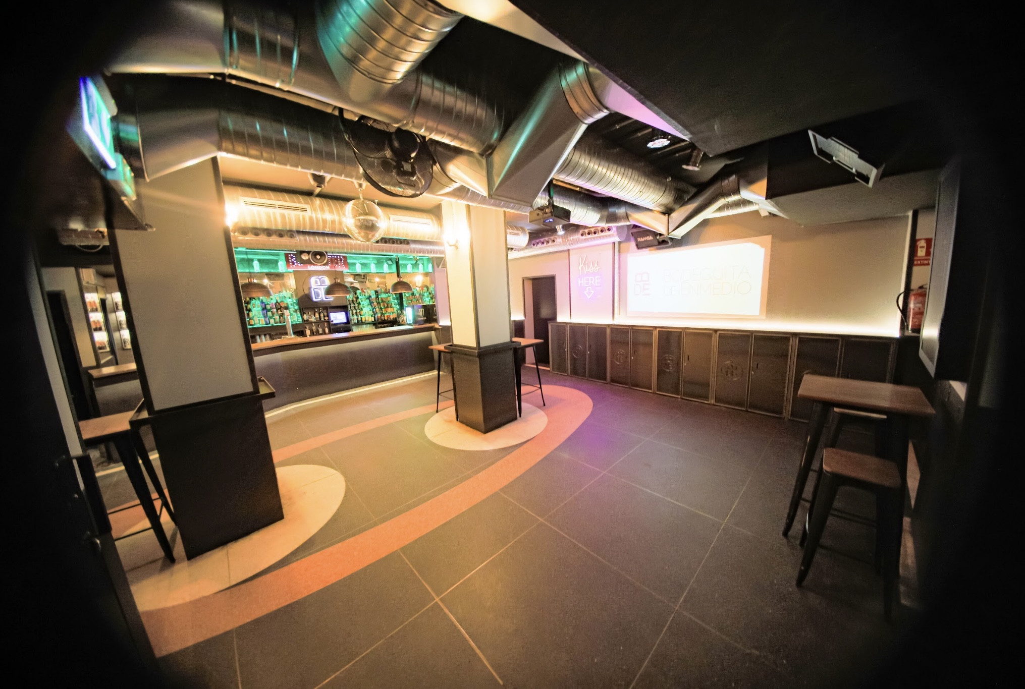 Interior de Bodeguita de Enmedio, con barra iluminada en tonos verdes, detalles industriales en el techo y un espacio amplio y moderno.