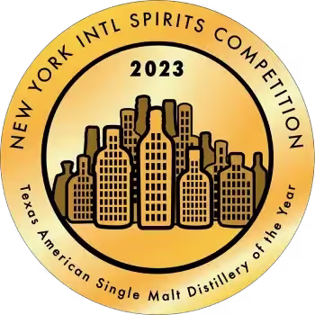 A gold circular badge reads New York Intl Spirits Competition 2023 and Texas American Single Malt Distillery of the Year, with an illustration of bottles in the center.