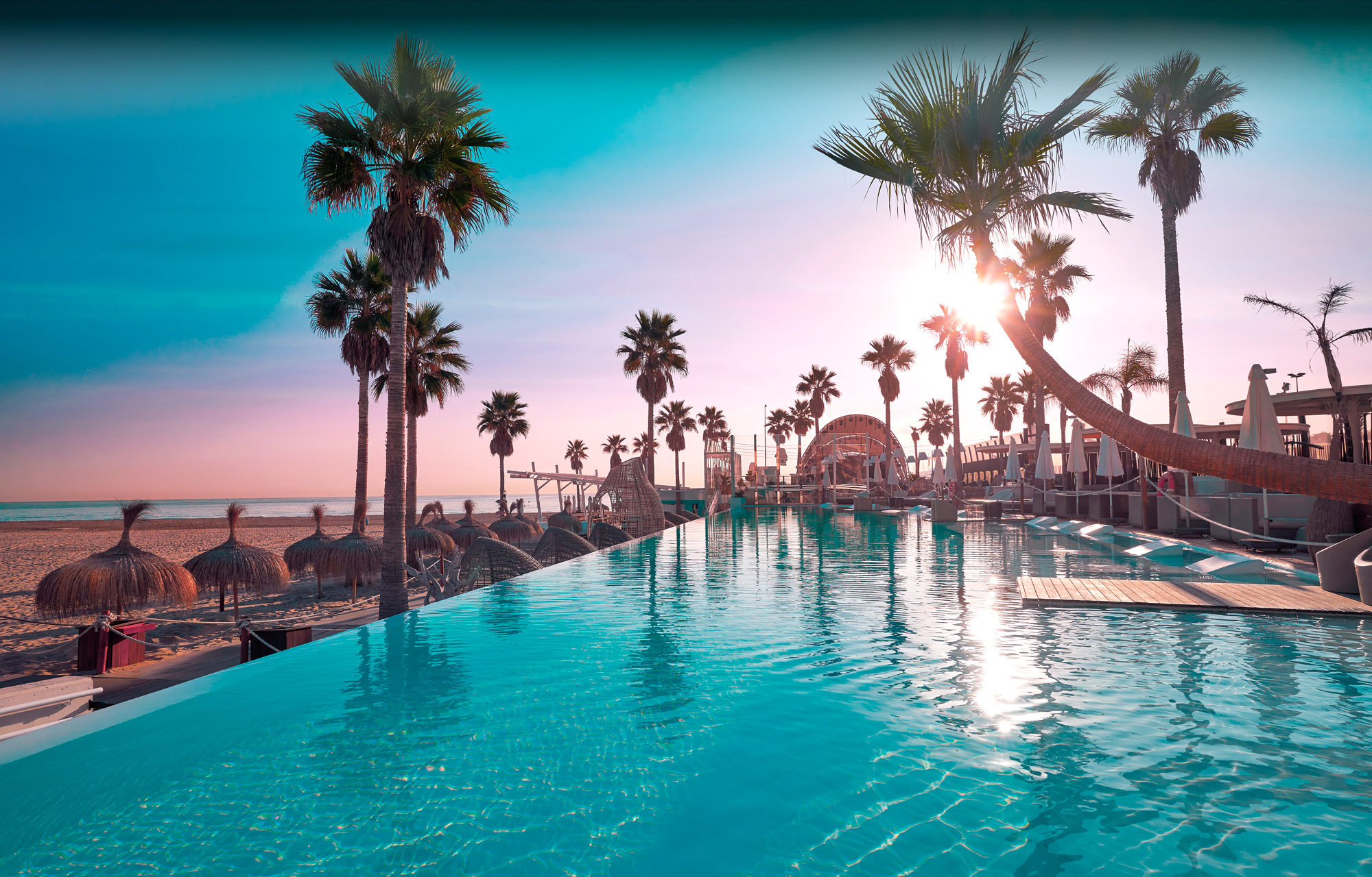 Marina Beach Club deslumbra con su infinity pool frente al mar, rodeada de palmeras y sombrillas, ideal para atardeceres de ensueño en Valencia.