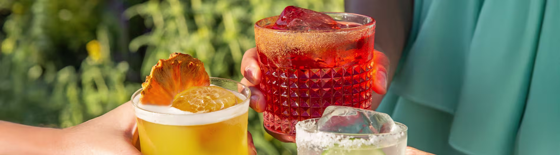 Trio of non-alcoholic cocktails held in a toast, with pineapple and citrus garnishes